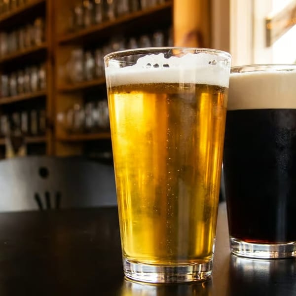 Two glasses of beer, one light and one dark, on a dark table in a pub setting.
