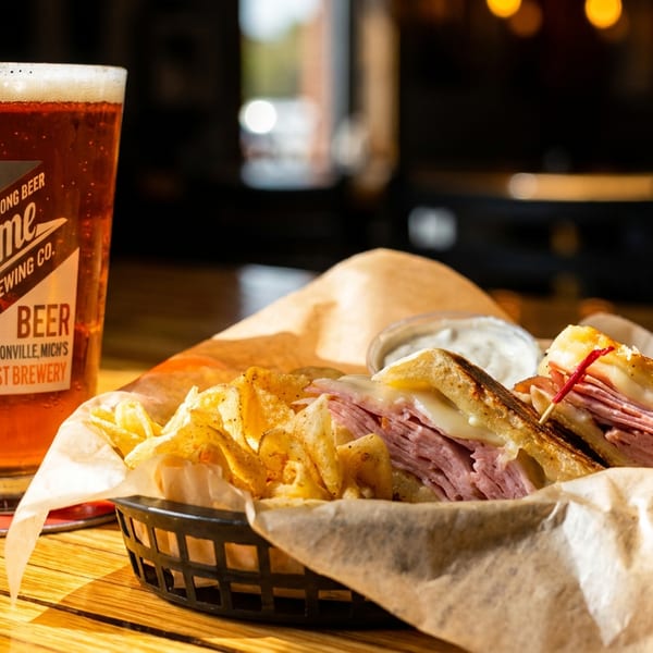 A White Flame Brewing Co. beer and a sandwich with chips in a basket on a wooden table.
