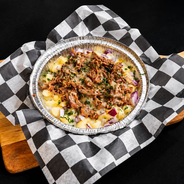 Pulled pork mac and cheese in a foil container on checkered paper and a wooden board.