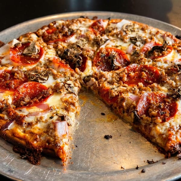 A whole pepperoni, sausage, mushroom, and onion pizza with one slice removed on a metal pan.
